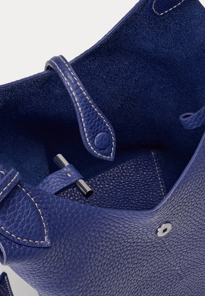Close-up of a blue textured leather bag with visible stitching, a buttoned strap, and a metal toggle closure inside the bag.