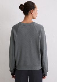 Szara, miękka bluza z polaru z raglanowymi rękawami, szerokim dekoltem i ściągaczem u dołu. Teksturowane wykończenie z minimalną liczbą szwów.