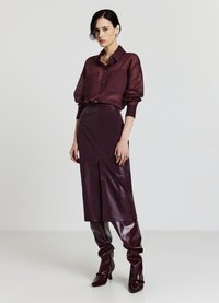 Chemise transparente bordeaux à boutons avec manches longues, associée à une jupe en cuir ajustée et des bottes en cuir brillantes montant jusqu'aux genoux, mettant en valeur une silhouette élégante.