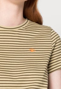 Randig t-shirt med korta ärmar i olivgrön och beige med rund hals. Har en liten broderad soldetalj i orange.