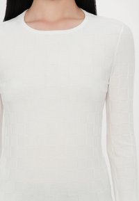Witte blouse met lange mouwen en een gestructureerd vierkant patroon. Heeft een ronde halslijn en een aansluitende silhoutte, gemaakt van een zachte, lichte stof.