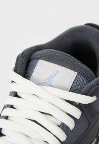 Grå atletiksko med hvide snørebånd, lavet af mesh og suede materialer. Har et logo-patch og teksturerede accenter på overdelen. Nærbillede.