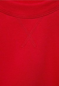 Nahaufnahme des roten Sweatshirt-Stoffs mit geripptem Kragen und genähtem X-Detail unterhalb des Halsausschnitts.