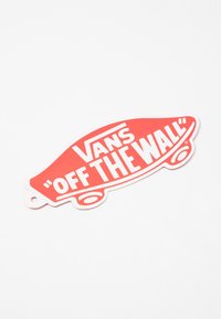 Étiquette logo « Off the Wall » de Vans rouge en forme de skateboard, avec un lettrage blanc audacieux sur une surface lisse. Trou pour suspension.