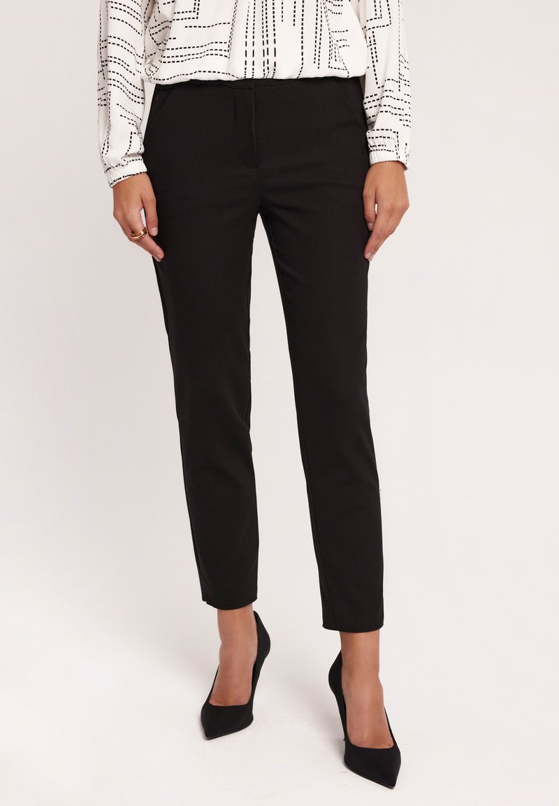 Czarne zwężane spodnie o gładkiej teksturze, z średnim stanem i bocznymi kieszeniami. Połączone z czarnymi szpilkami.