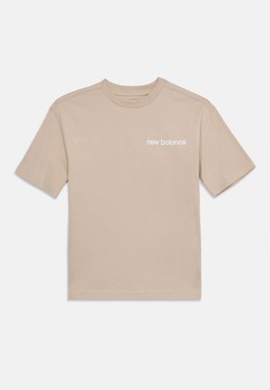 Beige lyhythihainen puuvillainen T-paita, jossa on valkoinen "new balance" -logo vasemmassa rinnassa.