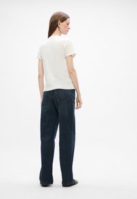 Hvid kortærmet t-shirt kombineret med mørke, løst siddende jeans. T-shirten har et simpelt design, og jeansene har baglommer.