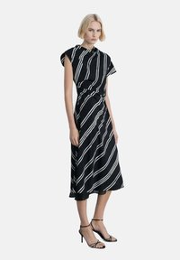 Robe midi à rayures noires et blanches avec des manches courtes, taille froncée et tissu fluide; associée à des talons noirs à lanières.
