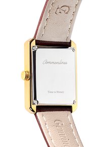 Rektangulært guldbag ur med indgraveret "Commonlines" og "Time is Money," med beige læderremme med præget tekst.