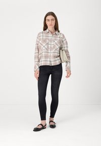 Camisa de botão xadrez em branco, rosa e verde, combinada com skinny jeans escuros e sapatos planos pretos. Inclui uma pequena bolsa cinza.