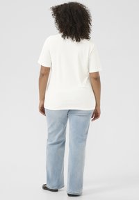 T-shirt blanc à côtes avec des manches courtes, associé à un jean droit bleu clair et des chaussures plates noires, vu de dos.