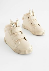 Chaussures pour tout-petits en cuir beige avec des bandes Velcro, ornées d'une bordure duveteuse et d'oreilles de lapin métalliques. Bout arrondi et semelle en caoutchouc texturée.