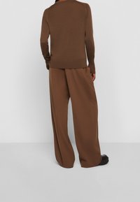 Pull en maille marron avec un col rond, assorti à un pantalon marron ample à jambes larges. Texture lisse, détails de couture subtils.