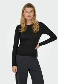 Svart langermet topp med rund hals og blonderdetalj. Mykt, tettsittende stoff kombinert med ensfargede, svarte bukser med vide ben.