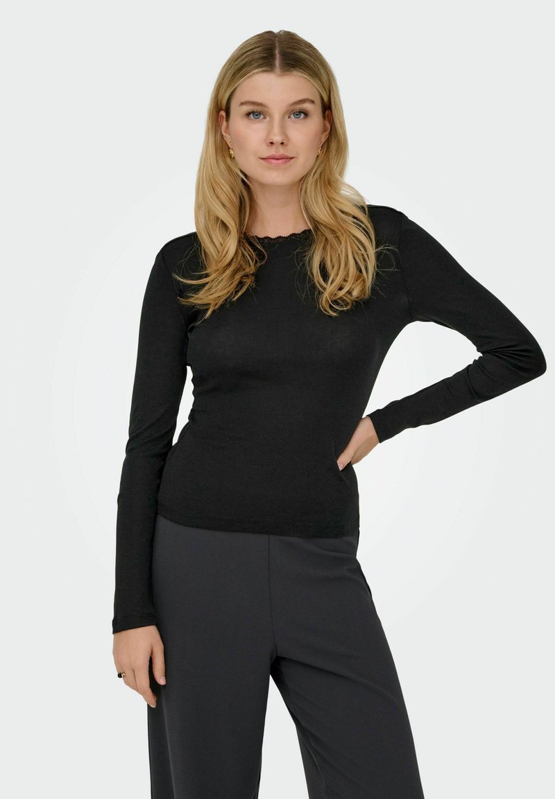 Svart langermet topp med rund hals og blonderdetalj. Mykt, tettsittende stoff kombinert med ensfargede, svarte bukser med vide ben.