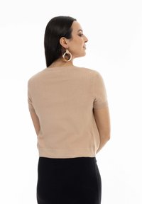 Maglione lavorato a maglia beige a maniche corte con scollatura rotonda e polsini a coste, abbinato a una gonna nera. Include grandi orecchini rotondi.