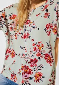 Blommig blus i ljusgrön tyg med röda, rosa och gula blommor, korta ärmar och en lös passform.