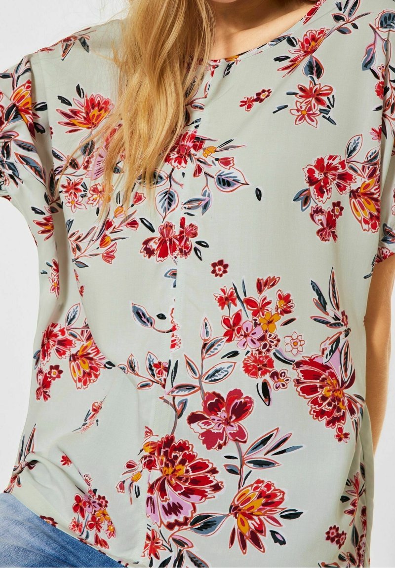 Blommig blus i ljusgrön tyg med röda, rosa och gula blommor, korta ärmar och en lös passform.