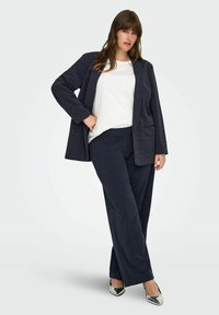 Temno moder blazer in usklajene široke hlače iz teksturirane tkanine, v kombinaciji z belo majico in srebrnimi čevlji.