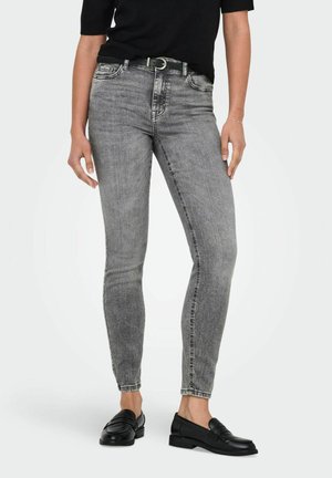 Graue enge Jeans aus Denim mit mittlerer Taille, fünf Taschen und einem ausgewaschenen Finish. Kombiniert mit schwarzen Slippern und einem schwarzen Oberteil.