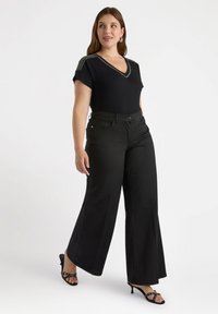 Black fitted top with V-neck and decorative bead accents on shoulders, paired with wide-leg black trousers and strappy black heels.