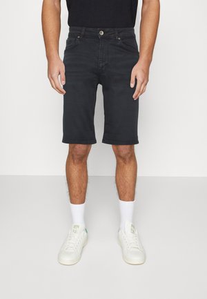 Donkerdenim shorts met een rechte snit, knoop- en ritssluiting, met vijf zakken. Draagt witte sokken en sneakers.