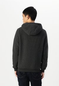Sudadera con capucha de felpa gris oscuro, con una superficie texturizada, capucha y puños acanalados. La parte de atrás muestra un ajuste relajado y no tiene logotipos visibles.