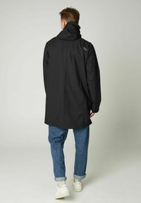 Schwarzer wasserdichter Mantel mit hohem Kragen, lockerer Passform und Kapuze, kombiniert mit blauen hochgekrempelten Jeans und weißen Turnschuhen. Einfaches Design, ohne Muster.