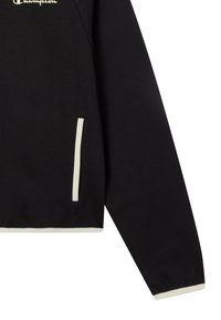 Czarna bluza z miękkiego materiału, z białym logo, kontrastowymi szwami, pół-zapięciem z przodu oraz bocznymi kieszeniami z białymi akcentami.
