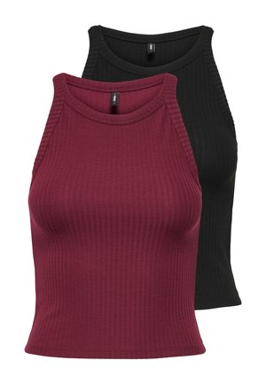 Jeune femme portant un haut sans manches bordeaux, un jean skinny noir, des ballerines bordeaux et portant un grand sac à bandoulière noir.