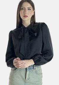 Sort satinbluse med bundet sløjfe ved kraven, pufærmer og indsamlede manchetter, kombineret med lyseblå denimnederdel. Glat tekstur, elegant design.