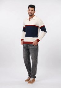 Pamut keverék pulóver tengerészkék testtel és krémszínű ujjal, piros részletekkel. Szürke farmerrel és világosbarna sportcipővel párosítva. Simább textúrájú.