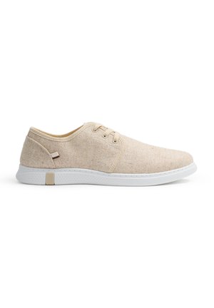 Zapatillas de tela beige con un acabado texturado, suela de goma blanca y diseño minimalista. Presentan acentos de franjas beige y marrón en el lateral.