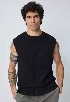 Pull sans manches en tricot noir avec une texture côtelée et un col rond, présentant des coutures visibles et une coupe décontractée.