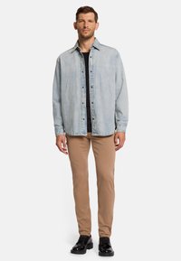Lichtblauwe denimshirt met knopen aan de voorkant, lange mouwen en klassieke kraag; gecombineerd met tan slim-fit broek en zwarte veterschoenen.
