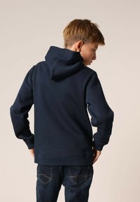 Donkerblauwe hoodie van zachte stof, met een achteraanzicht van een capuchon met trekkoord, geribbelde manchetten en tailleband, gecombineerd met spijkerbroek.