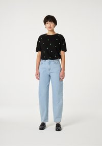 Zwarte korte mouwen t-shirt met groen bladerenprint, gecombineerd met lichtblauwe high-waisted jeans en zwarte instappers. Eenvoudige en casual look.