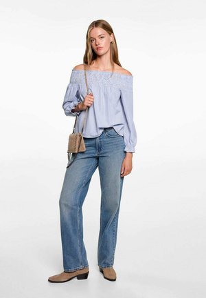 Blusa azzurra chiara con spalle scoperte e dettagli arricciati, abbinata a jeans blu a vita alta e stivaletti beige alla caviglia. Inclusa una piccola borsa a tracolla.