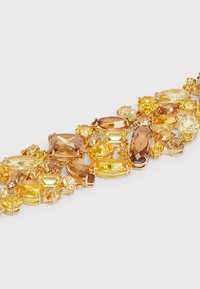Bracelet with large, faceted yellow, amber, and light brown gemstones set in gold-tone metal on a white background.