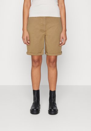 Shorts en coton kaki avec ourlets retroussés, dotés d'une poche ouverte et d'une texture lisse, associés à des bottines noires.