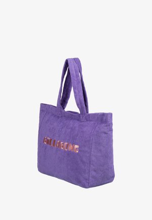 Lila corduroy-kangaskassi, jossa on kaksinkertaiset kahvat, etupuolella kohoava metallinen "BILLABONG" -logo ruusukultaisena, pehmeä rakenne ja vaorakenteinen muotoilu.