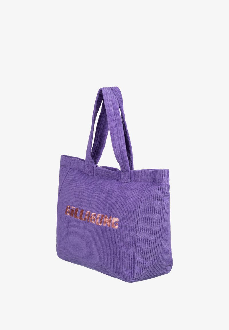 Fialová korduroy taška s dvoma rúčkami, má vystúpené kovové logo "BILLABONG" v ružovom zlate na prednej strane, mäkkú textúru a ryhovaný dizajn.