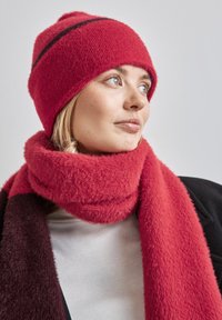 Berretto di maglia rosso e soffice con un accento a strisce nere; sciarpa spessa abbinata in una trama e tonalità simili; indossato con una maglietta bianca.