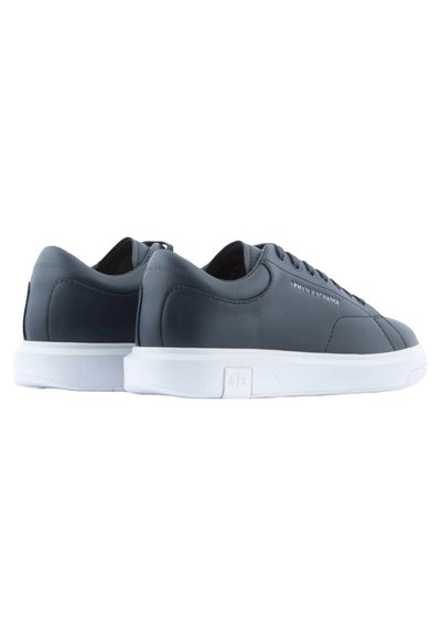 Baskets en cuir bleu marine avec semelle en caoutchouc blanche, bout rond et lacets plats. Présente un léger logo sur le côté et une texture lisse.
