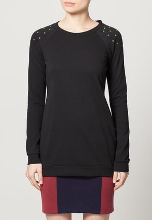 Maglietta nera a maniche lunghe con maniche raglan, caratterizzata da borchie verdi sulle spalle e un orlo testurizzato. Materiale in cotone morbido.