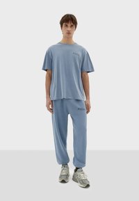 Svijetloplavi komplet loungewear-a koji se sastoji od opuštene majice s kratkim rukavima i odgovarajućih tapered hlača s mekim materijalom i diskretnim logotipom.