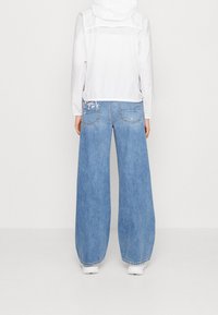 Blauwe wijde jeans met een lichtgewicht wit jack; zichtbare stiksels en twee achterzakken met lichte slijtage details.