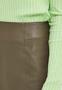 Gonna in pelle verde oliva con una texture liscia, dotata di tasca laterale e cuciture a contrasto, abbinata a una maglietta a righe verde chiaro.