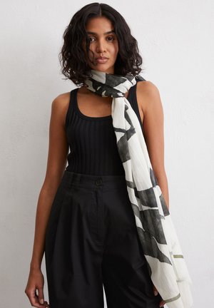 Leichter Schal in Creme mit abstrakten schwarzen Mustern. Lässig um den Hals getragen, kombiniert mit einem schwarzen gerippten Tanktop und hochtaillierten Hosen.