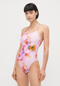 Én delig badedrakt i lys rosa med et lyst blomstermønster. Har tynne stropper og lav ryg. Laget av glatt, elastisk stoff.